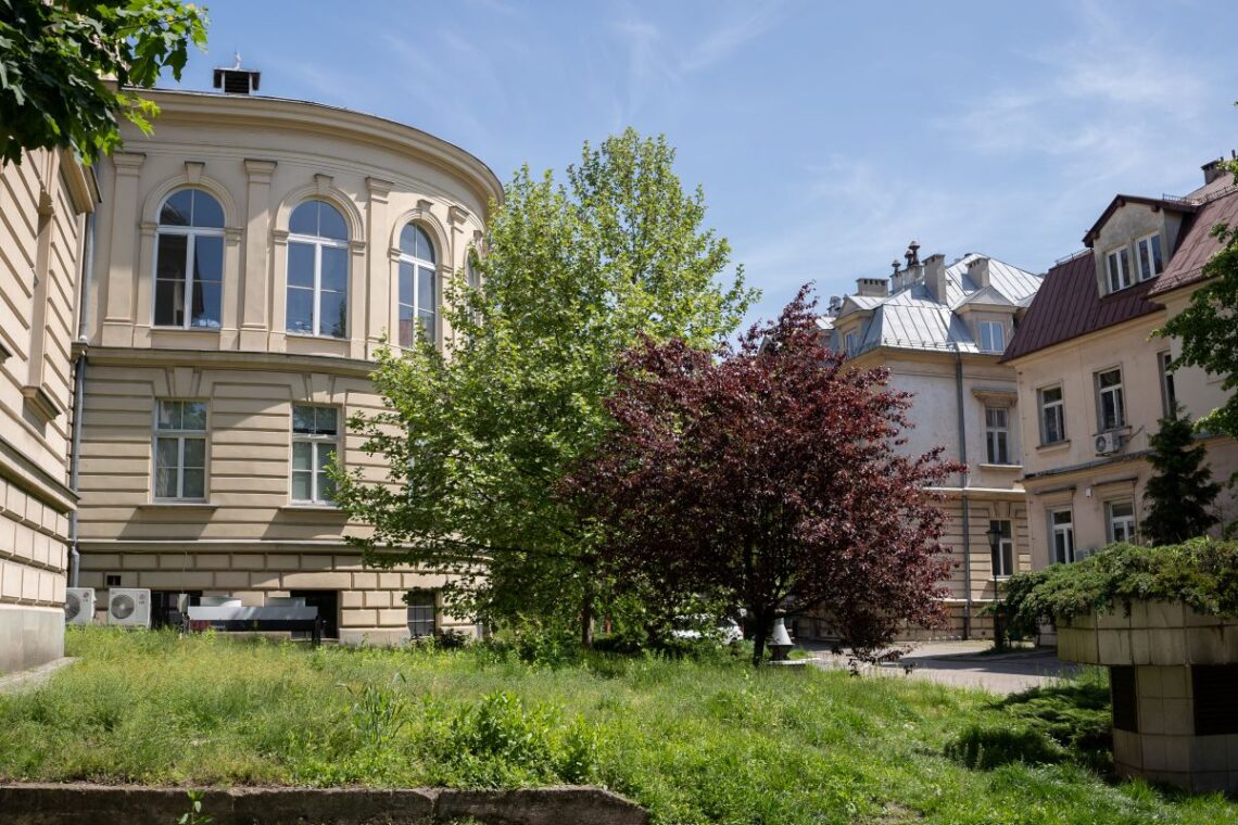 dwa stare budynki, między nimi rosnące drzewa i krzewy