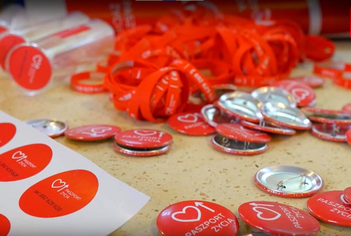 przypinki i smycze w kolorze czerwonym z symbolem "paszportu życia"