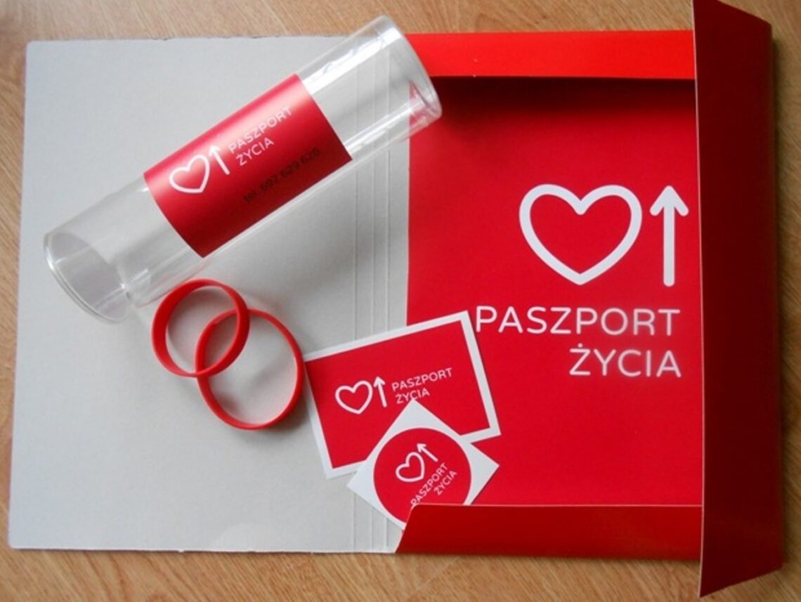 zestaw analogowy "paszportu życia": tubka z naklejką w kolorze czerwonym z symbolem "paszportu życia", naklejki i opaski silikonowe, czerwone, z napisem "paszport życia"
