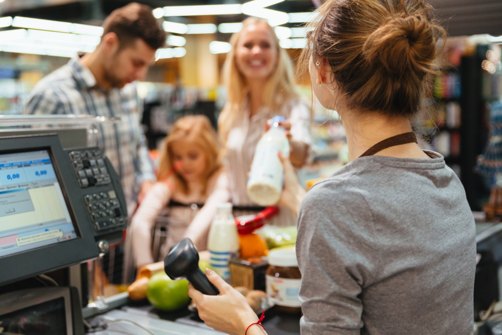 młoda kobieta przy kasie w supermarkecie obsługująca trzyosobową rodzinę