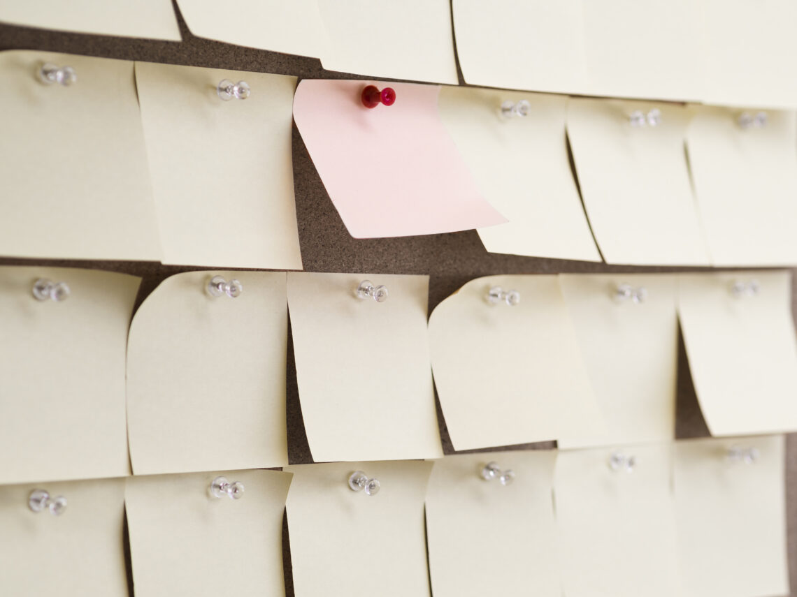 Na zdjęciu znajdują się małe karteczki post-it przyczepione do korkowej tablicy.