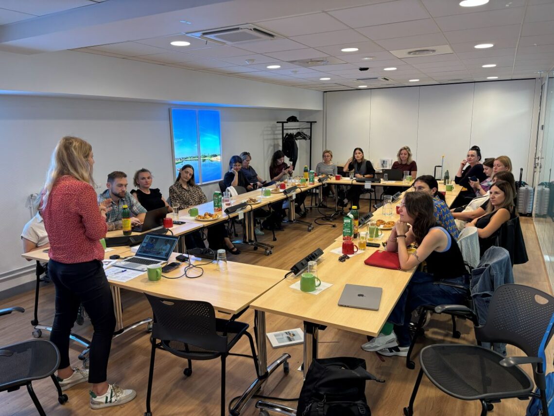 grupa ludzi słuchająca przy stołach ustawionych w czworobok, słuchająca wykładu