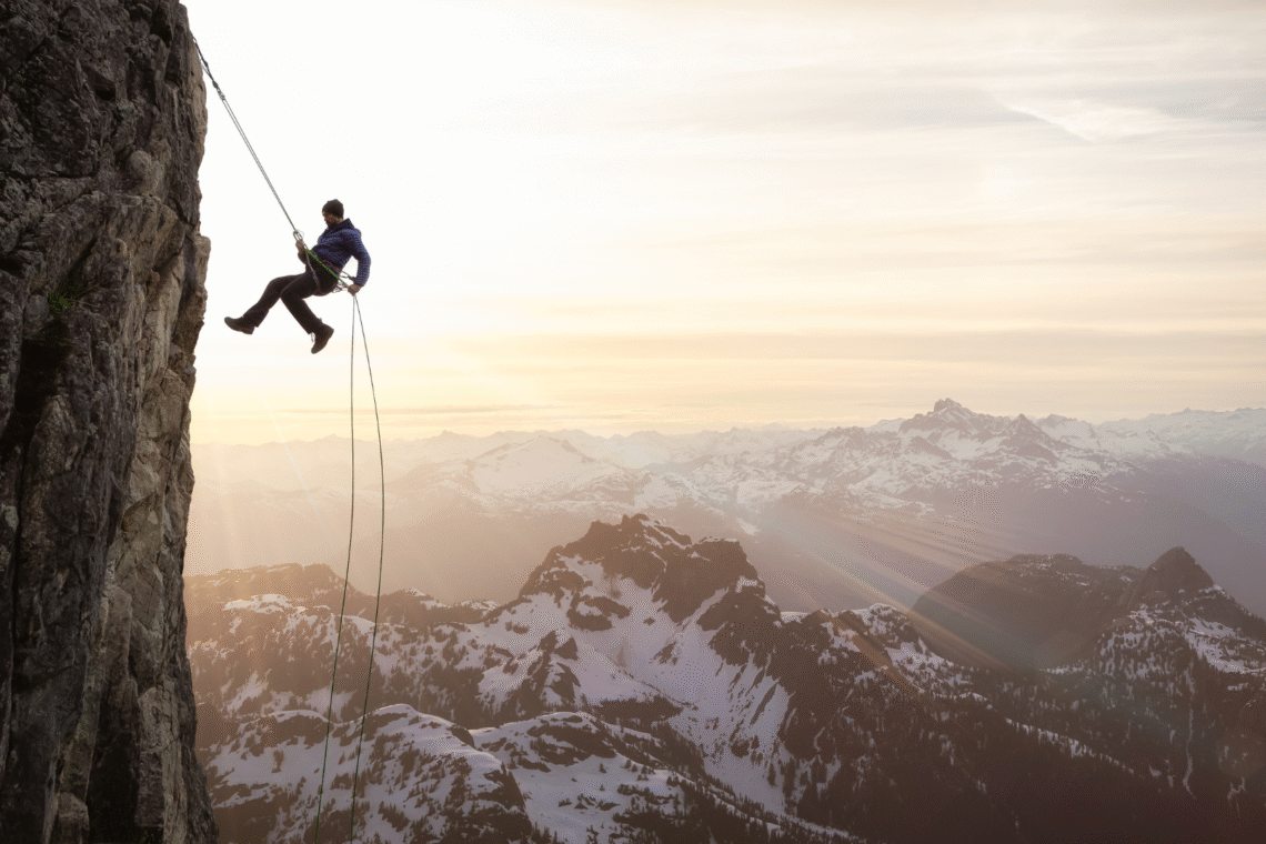Na zdjęciu jest mężczyzna w trakcie zjazdu po wspinaczce na górę.
