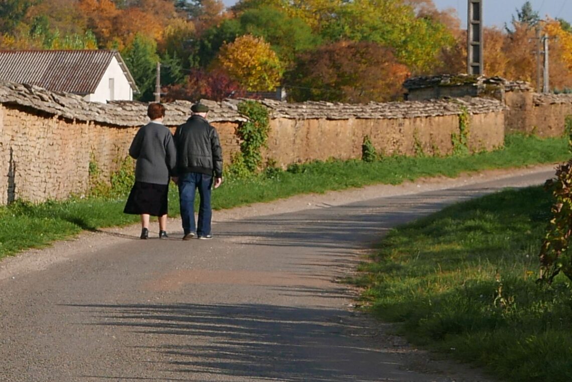 Dwoje seniorów idzie ulicą wzdłuż murku