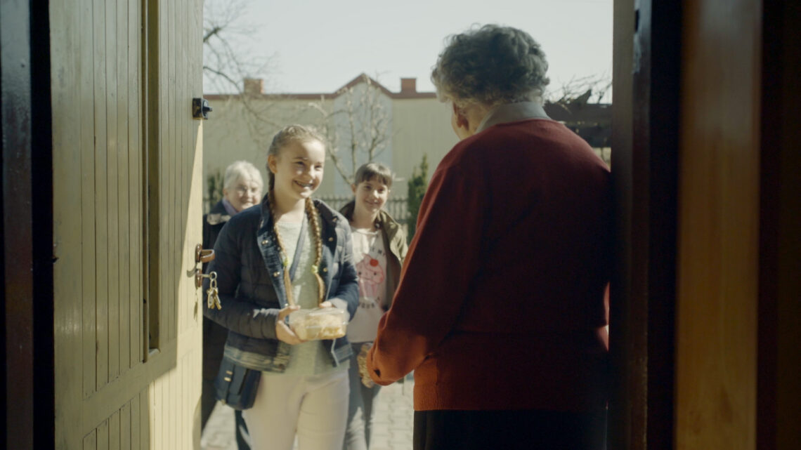 Seniorka stoi w drzwiach, a przed drzwiami grupa dziewczynek.