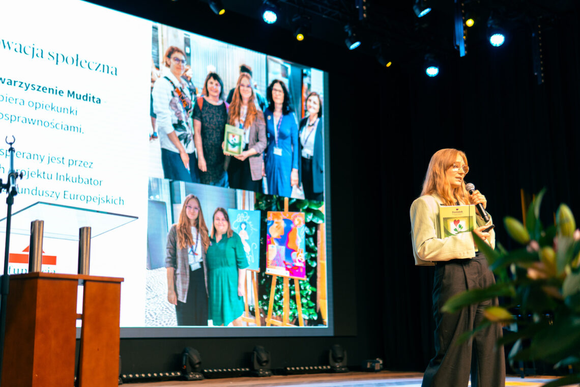 konferencja, w tle scena z wyświetlonym na ekranie zdjęciem Powitalnika, przez mikrofon mówi Marta Rutkiewicz