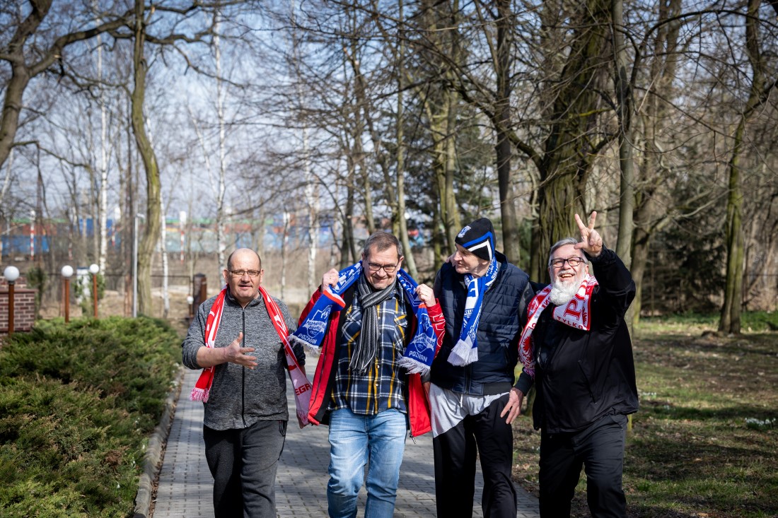 Czterech mężczyzn idących przez park w szalikach klubu piłkarskiego