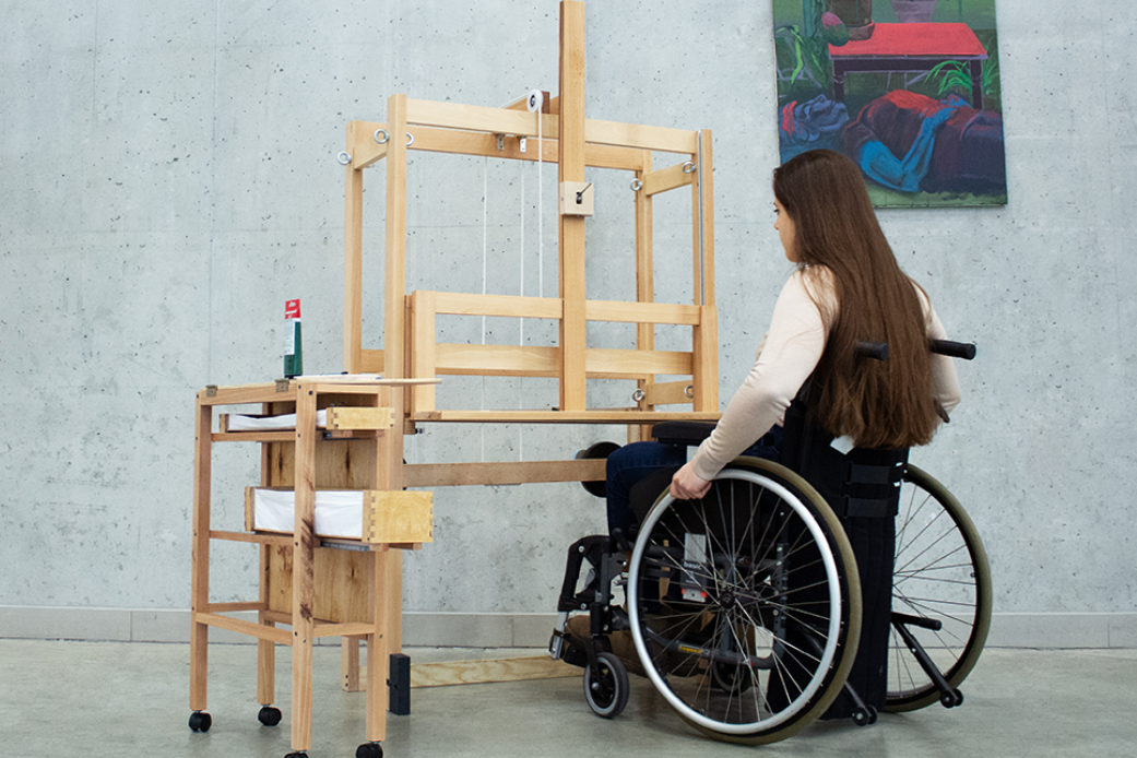 zdjęcie: kobieta na wózku przed sztalugą o specjalnej konstrukcji