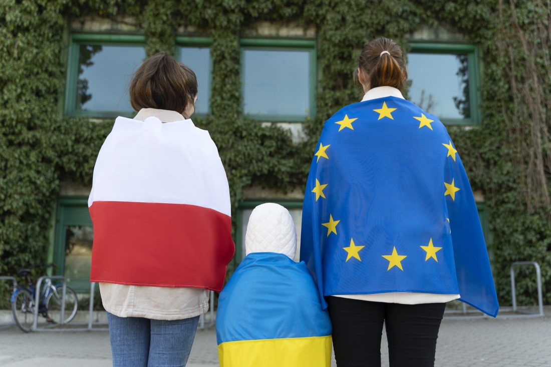Troje ludzi odwróconych plecami z flagami kolejno: Polski, Ukrainy i Unii Europejskiej