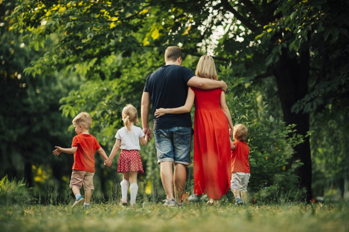 Zdjęcie rodziny tyłem, na zdjęciu rodzice i troje dzieci, idą trzymając się za ręce