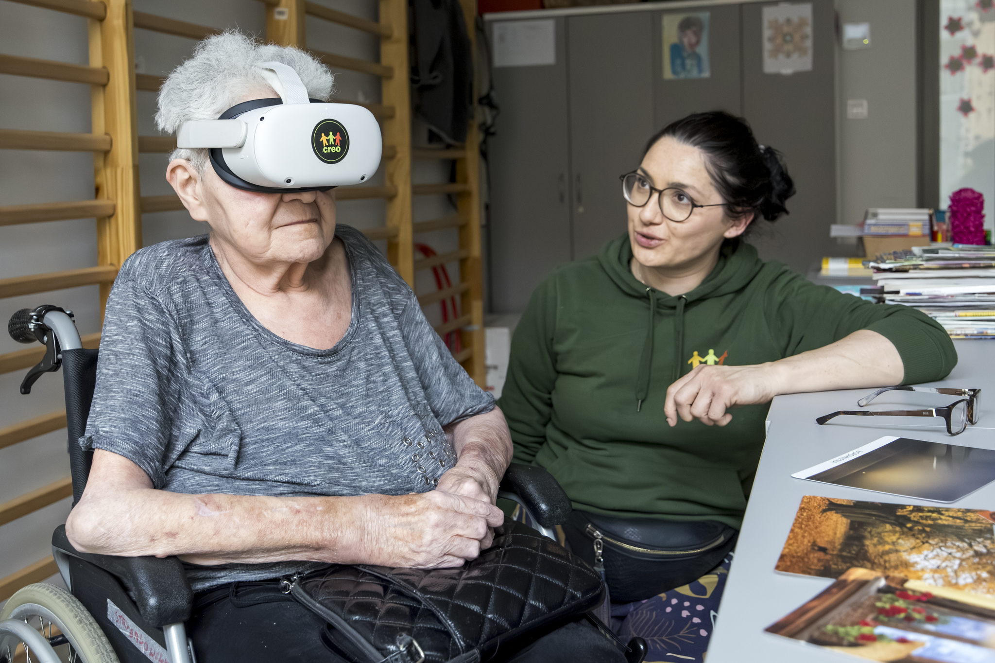 Młoda kobieta, animatorka wraz z seniorką, uczestniczką zajęć. Seniorka ma na sobie gogle VR