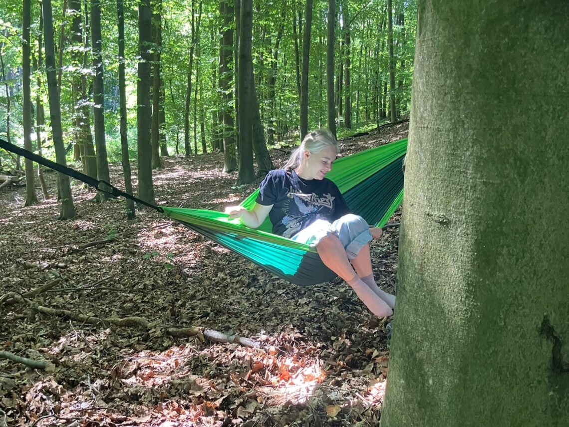 kobieta siedząca na hamaku rozpiętym między drzewami w lesie