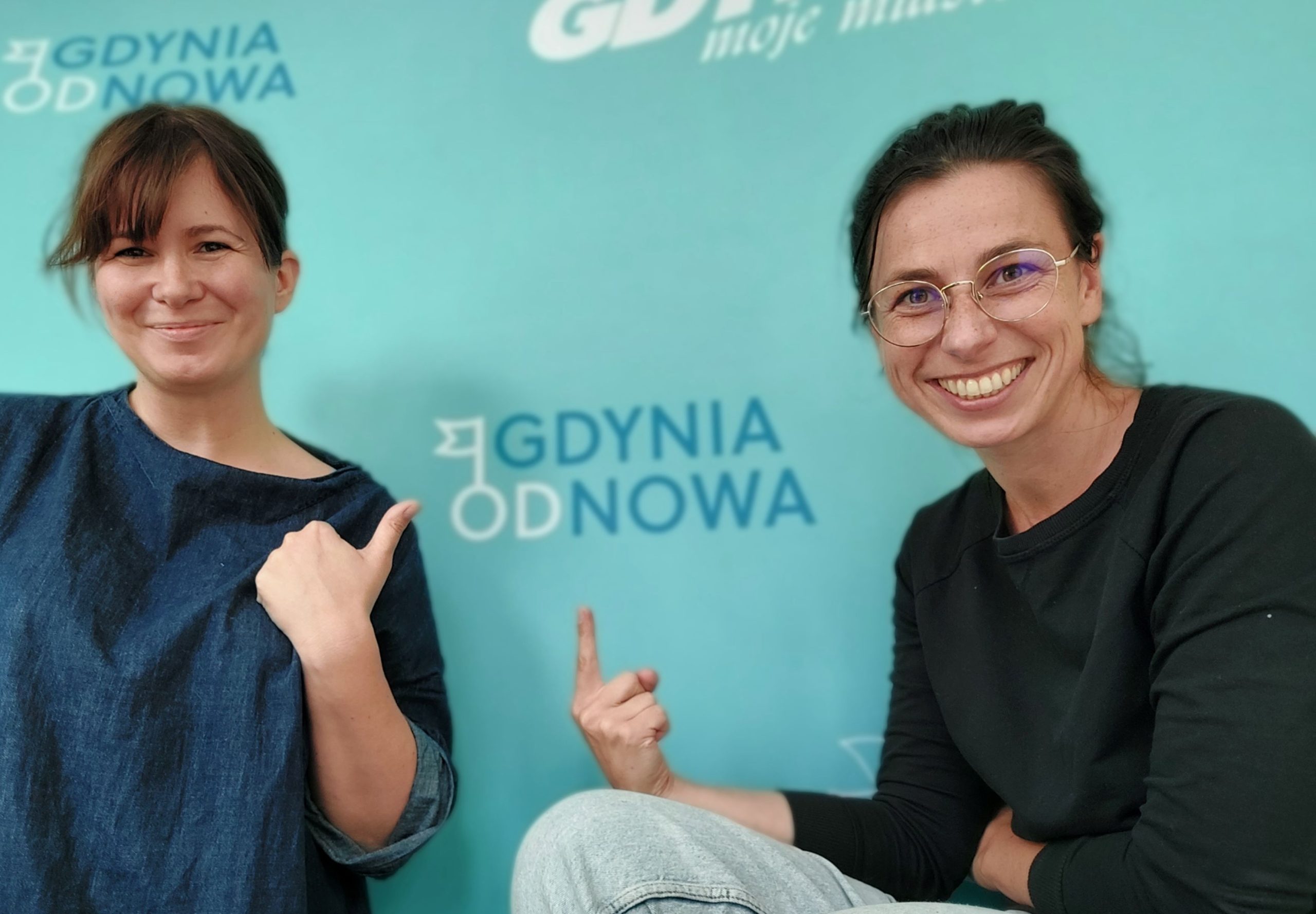 dwie uśmiechnięte kobiety wskazujące kciukami na napis Gdyni ODnowa