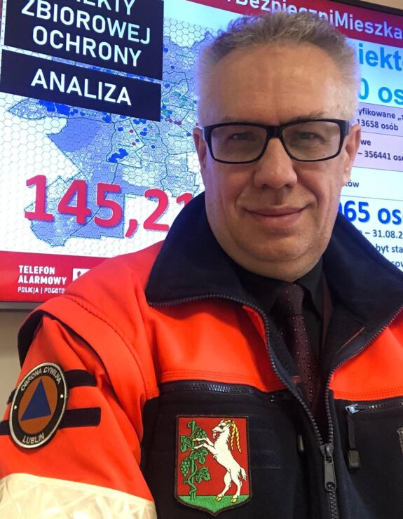 Pan w okularach, ubrany w uniform służb zarządzania kryzysowego z herbem Lublina na piersi