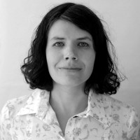 Czarno-biały portret kobiety z ciemnymi, falowanymi włosami do ramion, ubranej w jasną koszulę.